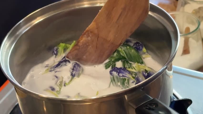 Stirring a Pot of Coconut Milk with Butterfly Pea Flowers to Make Thai Sticky Rice with Mango