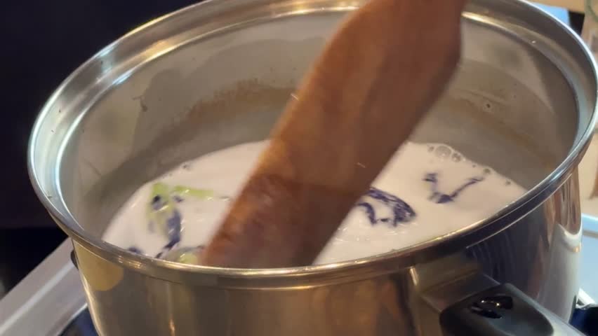 Stirring a Pot of Coconut Milk with Butterfly Pea Flowers to Make Thai Sticky Rice with Mango