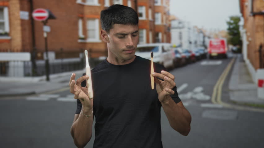 Man holding electric toothbrush and bamboo toothbrush while comparing oral care tools on street; sustainable hygiene curiosity.