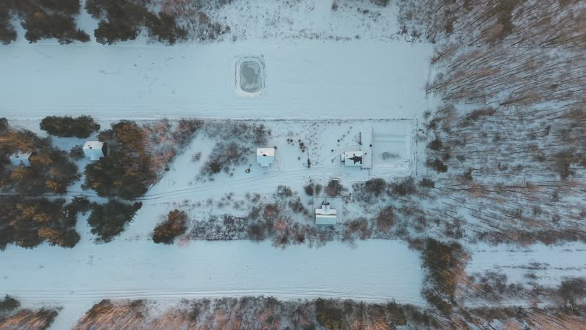 Top-down panning drone fly over snowy hidden community area cutting through forest landscape in winter, Helenow, Lipsko, Poland