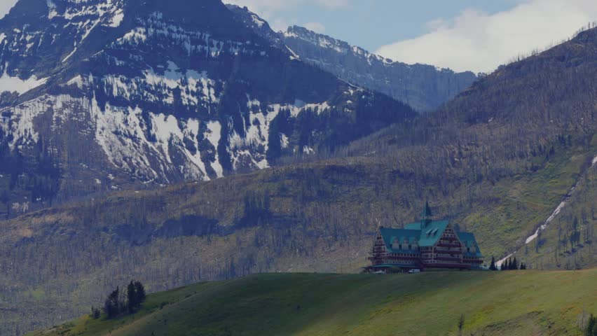 Prince of Wales Hotel standing on a green hill with snow capped mountains in Waterton national park