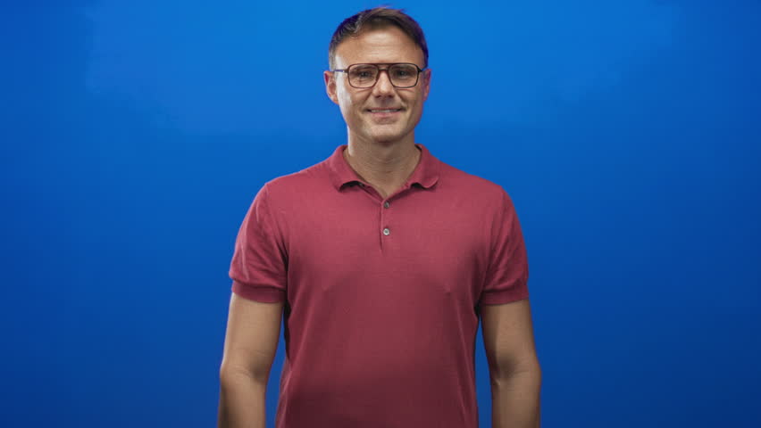 Man clapping hands in a studio with blue wall, wearing glasses and red polo shirt; warm approval encouragement.