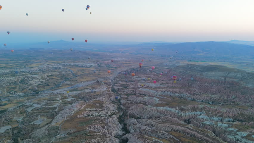 Goreme, Nevsehir, Turkey. Massive fleet of hot air balloons with fire bursts flying over Cappadocia plateau and valleys in clear morning with blue haze at sunrise. Aerial View