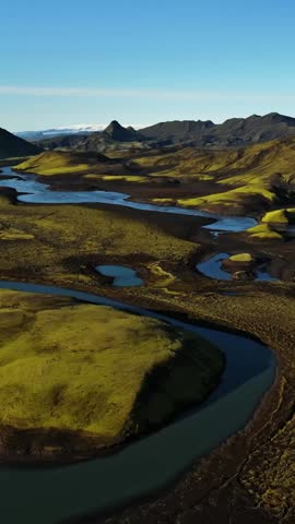 Wide drone panorama of Iceland highlands with winding glacial river, mossy lava banks and dark volcanic plains under clear sky, perfect for cinematic travel and nature backgrounds.