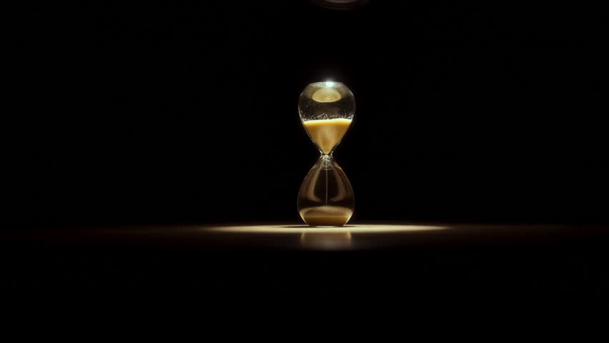 Close-up photograph of golden glittering sand leaking out of an hourglass.