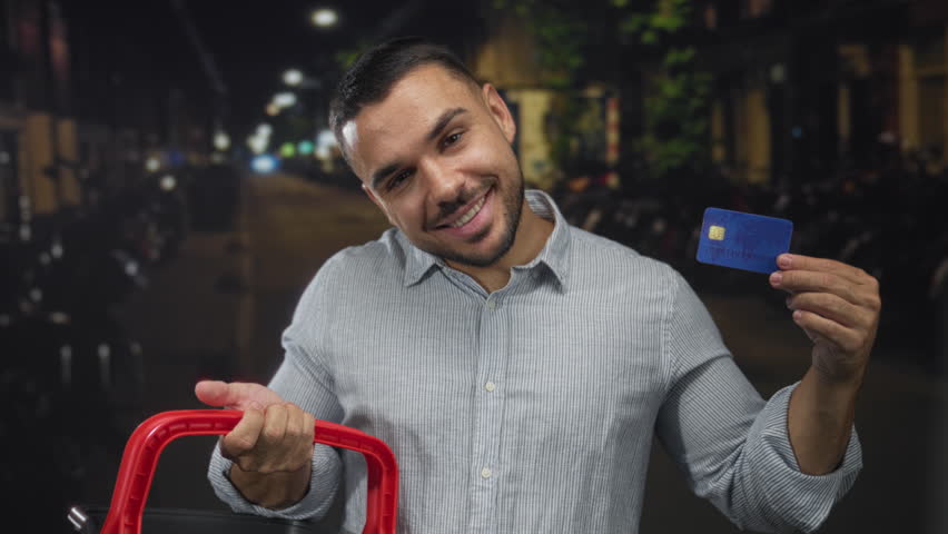 Man holding blue creditcard and red trolley handle on street at night; financial confidence money management.
