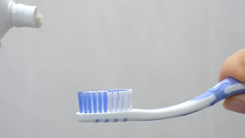 A woman applies toothpaste to toothbrush on gray tile background close up.