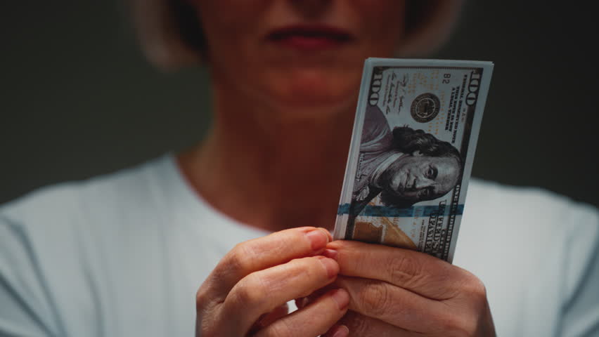 Old Caucasian woman counts the cash one hundred in hands, banknotes. Senior female holds paper money USD dollars in palms, with money deficit. Utility Bills Payment earnings. Elderly lady counting.