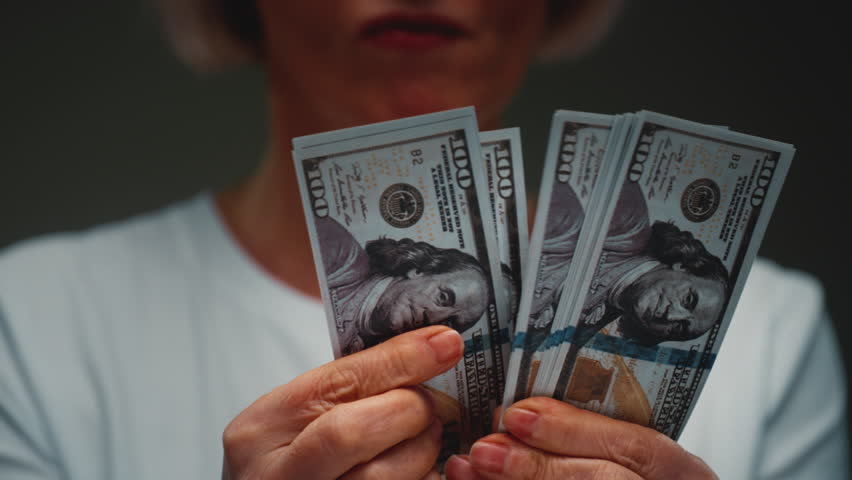 Old Caucasian woman counts the cash one hundred in hands, banknotes. Senior female holds paper money USD dollars in palms, with money deficit. Utility Bills Payment earnings. Elderly lady counting.