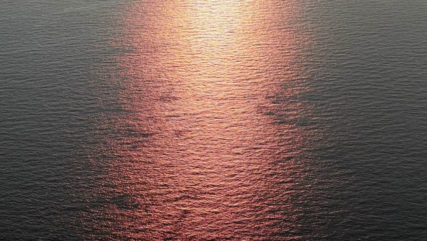 Aerial shot highlights golden sunset over the sea, waves glowing with radiant light and tranquil beauty.