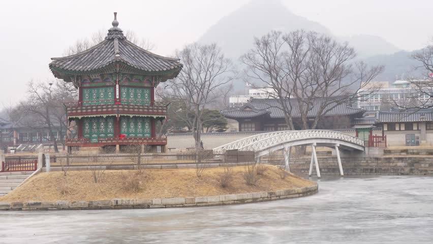 Slow motion landscape of Hyangwonjeong Pavilion temple with bridge spanning across frozen lake near the Secret Garden within Gyeongbokgung Palace grounds in Seoul South Korea Asia travel and tourism
