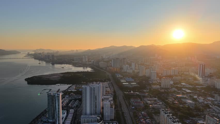Aerial view nighttime aerial view of George Town skyline, coastline, bridge, highway and surrounding hills under glowing sky.