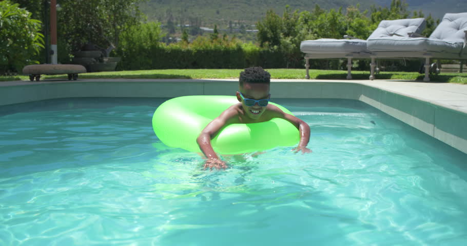 African American male youth leaning through neon-green ring, paddling in backyard pool cooling off. Inflatable, goggles, water, joy, outdoor, sunny, summer