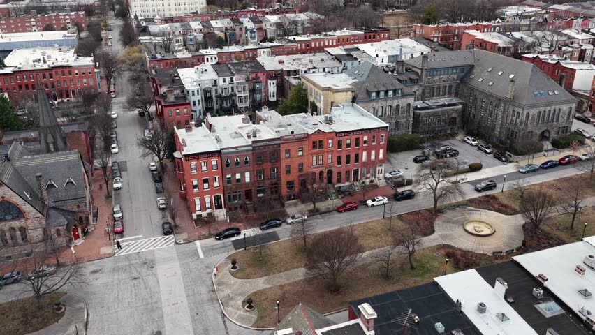 Aerial view of Baltimore’s Bolton Hill neighborhood in winter, with historic brick townhouses, a large stone church and quiet residential square with leafless trees and parked cars. Approaching shot.