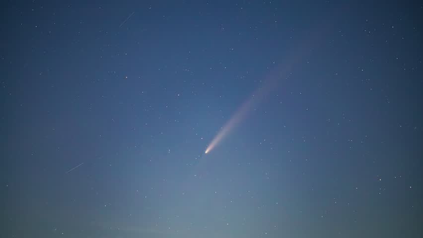 A comet descends into a blue starry sky during a time lapse recording.