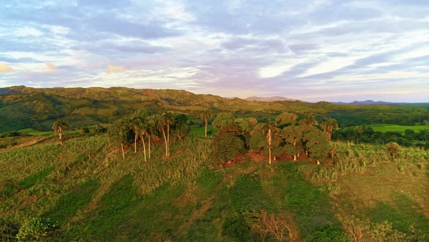 Mountain valley in the rays of the setting sun. Evening landscape of mountain peaks against a cloudy sky. Beautiful scenery with forests, hills, and meadows in the evening light. A ridge with a high peak in the distance.