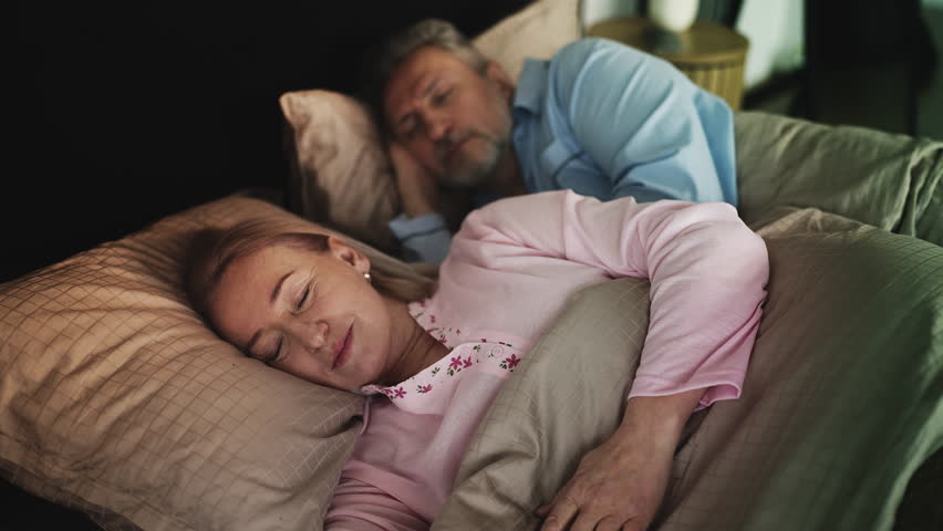 Happy middle-aged couple peacefully sleeping embraced in bed, healthy night rest