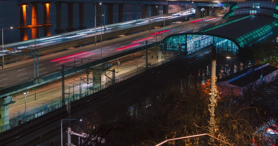Tilt up hyperlapse fast traffic light trails on Gangbyeonbuk-ro expressway, metro trains arriving Oksu Station, illuminated Donho Bridge, Han River reflections, glowing city skyline, silhouetted mount