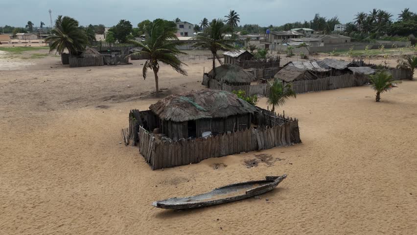 Cinematic drone shot of the tropical coastline in Lome, Togo. Features rolling waves, a wide sandy shore, and the vast Atlantic horizon under an overcast sky