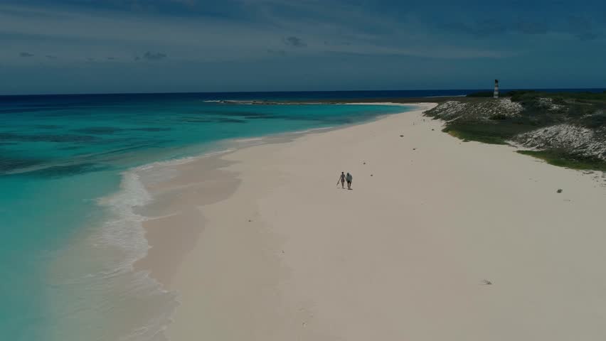Aerial view of a couple walking holding hands on the white sand beach of Cayo de Agua in the Los Roques Archipelago, Venezuela, with turquoise Caribbean waters and a tropical paradise setting