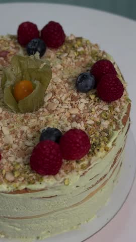 A beautifully decorated layered cake with raspberries, blueberries, and nuts, displayed on a white plate against a soft background
