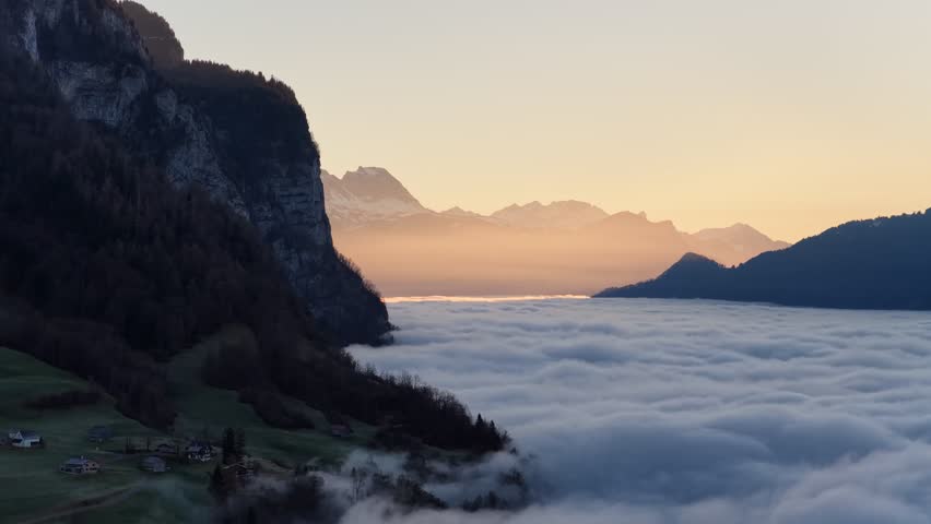 Aerial drone view of mountain cliffs rising above clouds at Walensee Switzerland