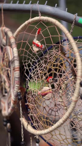 A dream catcher is hanging from a fence. The dream catcher is decorated with beads and has a bird on it