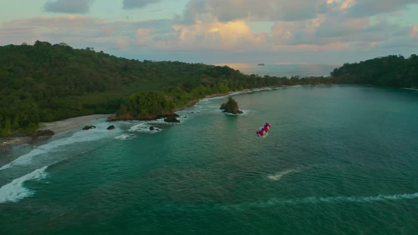 Drone view of parasailing during sunset at Manuel Antonio National Park Costa Rica, surrounded by lush shoreline, stunning beach and turquoise blue ocean