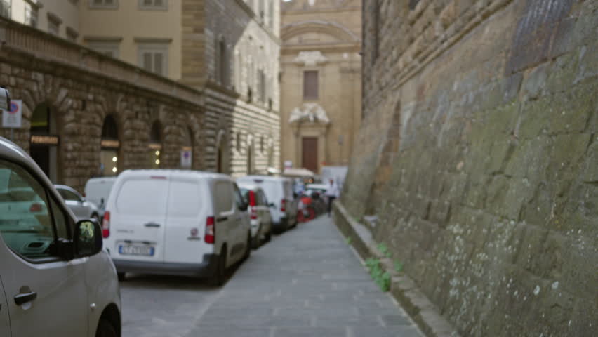 Narrow florence street with parked vans and textured stone wall in soft defocused bokeh; background backplate copyspace calm.