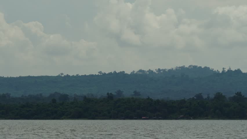 Close up view of clouds moving above tropical mountinous landscape with lake in the foreground.