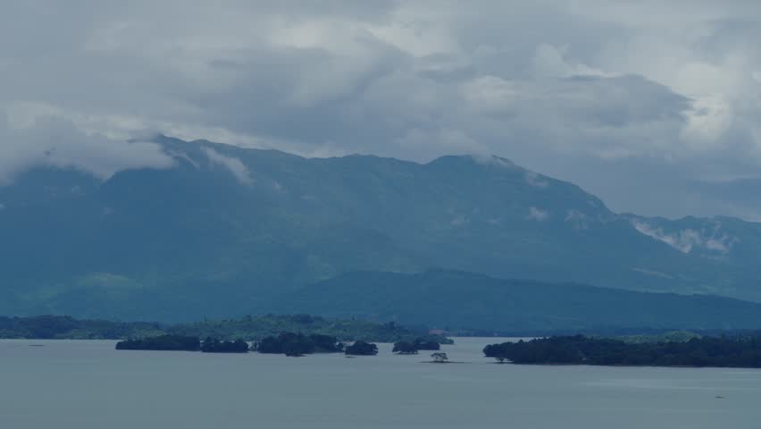 Panning slow close up view of clouds moving above tropical mountinous landscape with lake in the foreground.