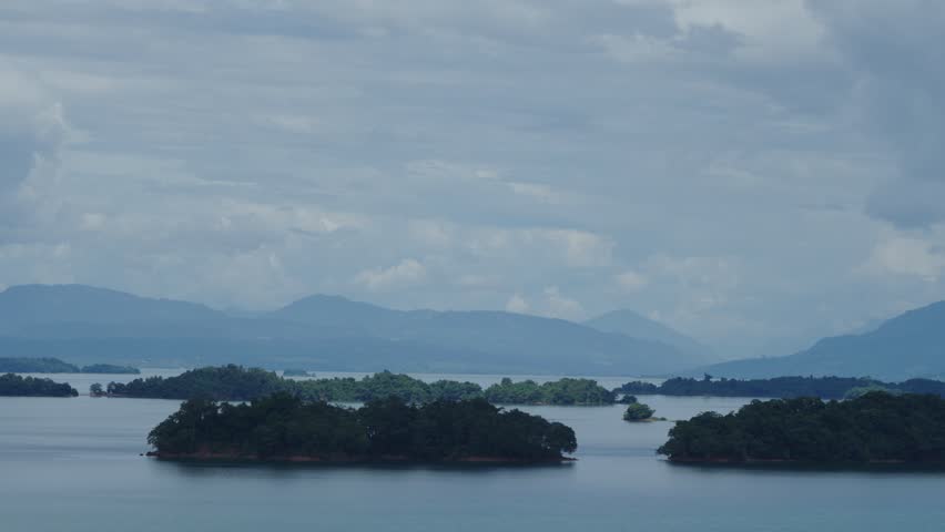Sideward panning slow close up view of clouds moving above tropical mountinous landscape with lake and sporatic islands in the foreground.