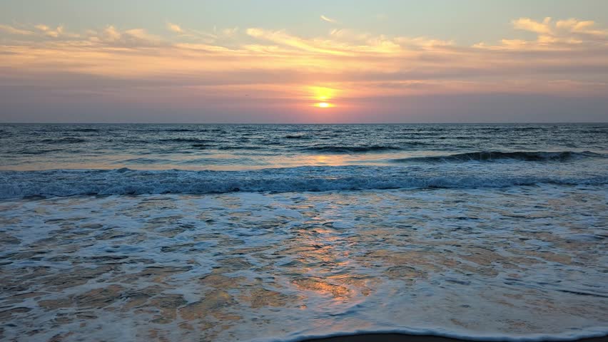Morning sun shining behind clouds over calm sea waves in peaceful and atmospheric coastal scene