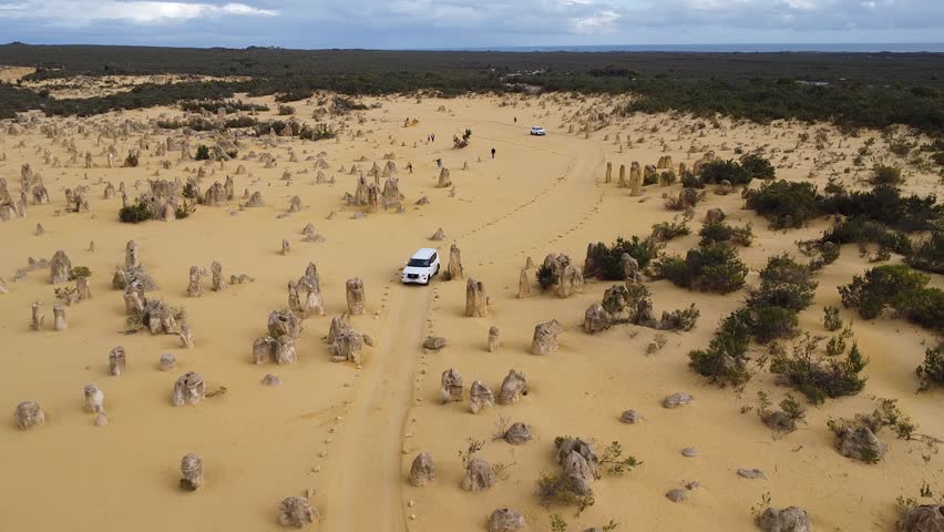 Cinematic aerial panorama of The Pinnacles Desert, highlighting unique limestone spires rising from golden sands in Nambung National Park, Western Australia.
