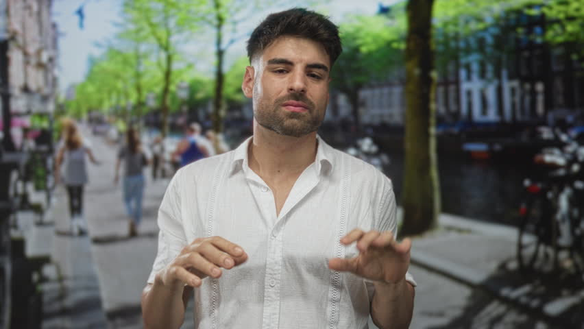 Young hispanic man covers face with hands on sunny urban street and gestures rejection; frustration.