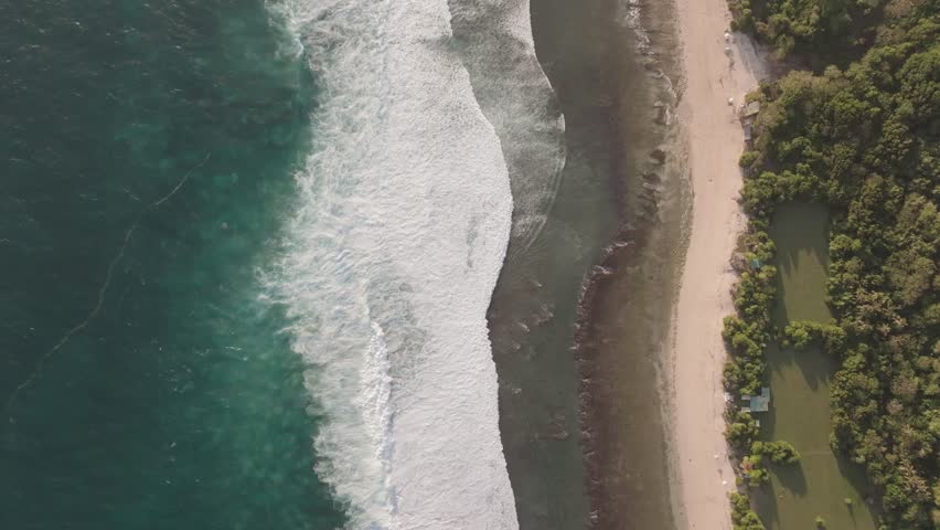 A 4k drone shot of the Bali shoreline with the crystal blue ocean on one side and a tropical green coast on the other