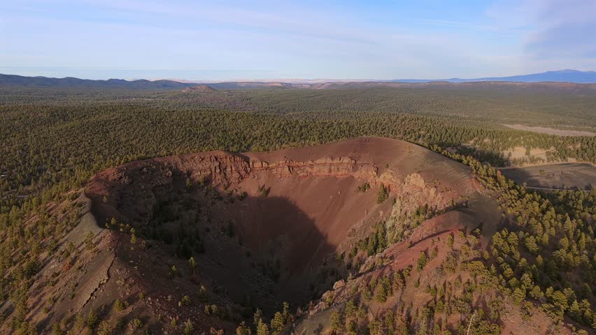 A dramatic drone perspective of a dormant cinder cone volcano, revealing a deep, tree-lined crater. This 4K shot highlights the rugged geological scale of a remote volcanic wilderness.