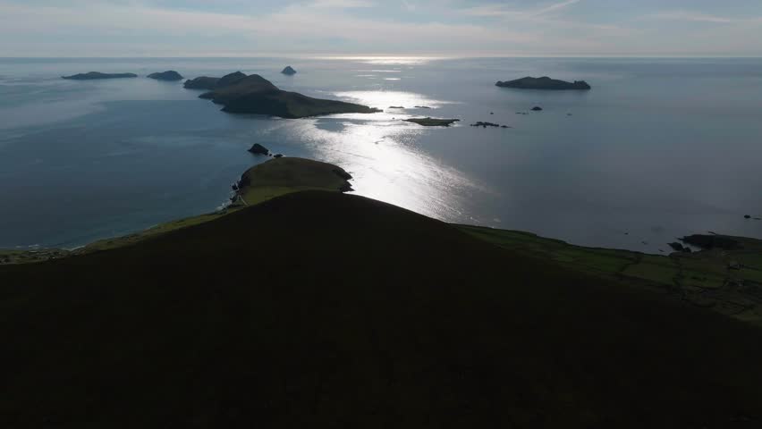 Stunning drone footage capturing the Great Blasket Island and Atlantic Ocean from a mountain top in County Kerry, Ireland, featuring shimmering sun reflections.