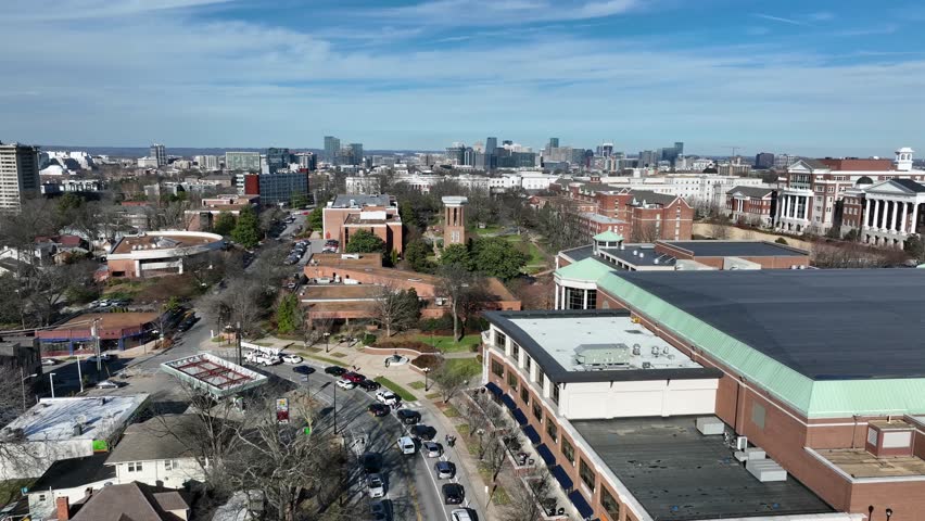 Aerial flyover of Belmont University in Nashville, Tennessee, with red brick campus buildings, bell tower and downtown skyline in distance under clear sunny winter sky. Wide shot.
