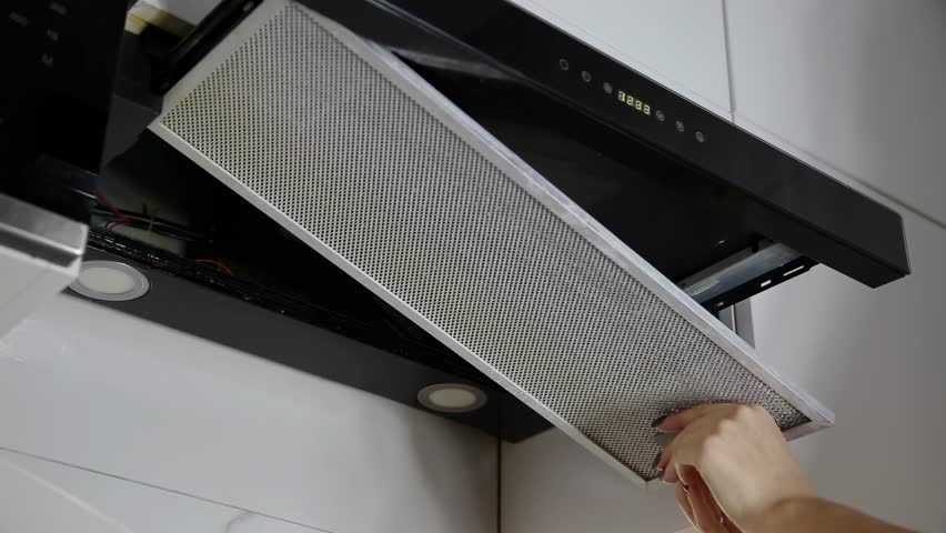 Close up view of woman hands working on kitchen appliance. Installation of a clean metal filter into an exhaust fan. White tile and modern design for home care.