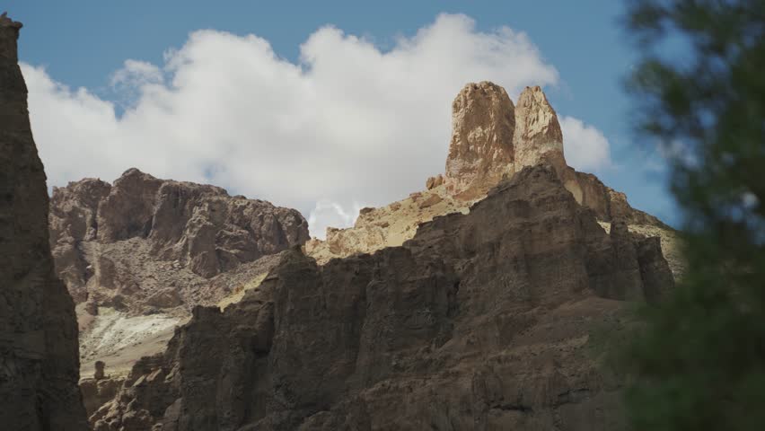 Volcanic rock towers and jagged mountain ridges under a bright blue sky with blurred image of hiker passing by