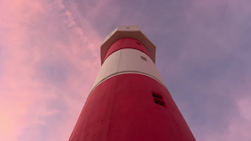 low-angle shot looking up at a tall, majestic lighthouse against a beautiful sunset sky