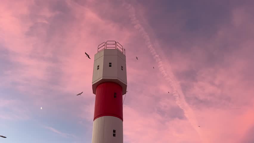 shot looking up at a tall, majestic lighthouse against a beautiful sunset sky