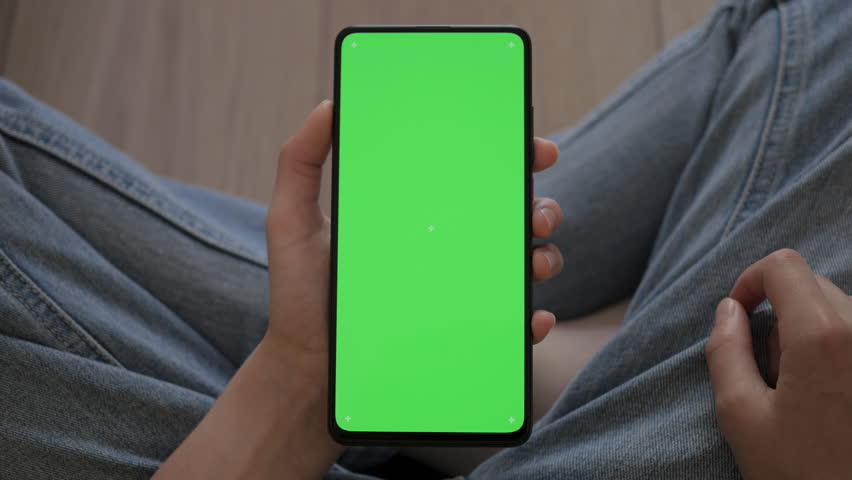 Child at Sitting on Floor in Living Room Using Phone With Green Screen Mock-up. Phone With Green Mockup Screen Chroma Key Internet Watching Content Videos Blogs Learning. Girl Playing Video Games.