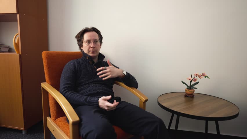 A man wearing glasses sits in a chair and converses with his counterpart. An important educational conversation in the study.