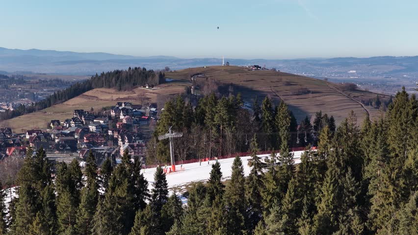Aerial drone view of Koziniec ski slope on Czarna Gora in Zakopane and Poronin area, showing snowy pistes, skiers, chairlift and panoramic Tatra Mountains landscape on a clear winter day	