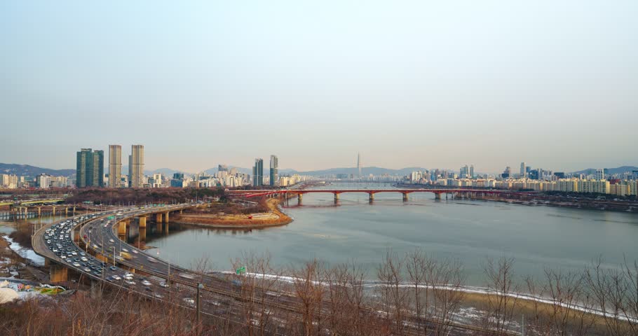 Aerial time lapse heavy traffic flow on curving Gangbyeonbuk-ro expressway with Seongsu Bridge and distant Lotte Tower during winter sunset transition to night in Seoul South Korea
