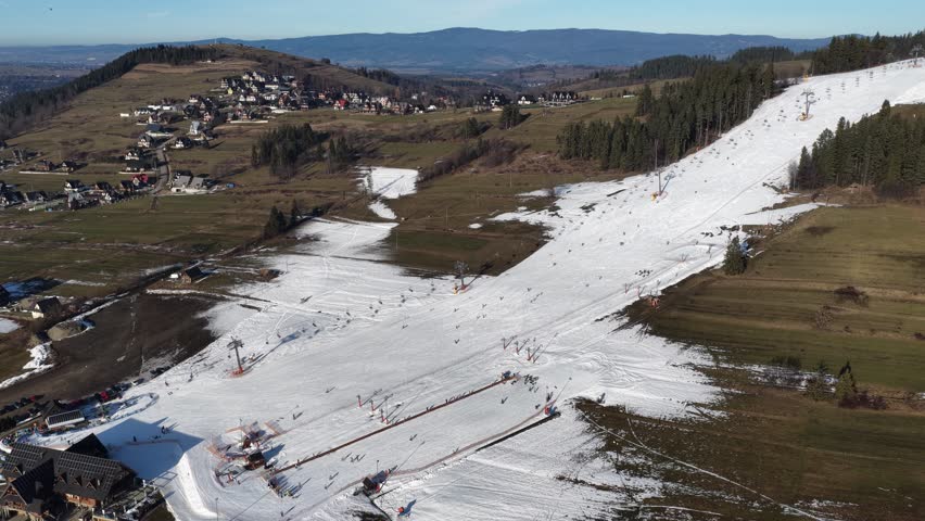 Aerial drone view of Koziniec ski slope on Czarna Gora in Zakopane and Poronin area, showing snowy pistes, skiers, chairlift and panoramic Tatra Mountains landscape on a clear winter day	
