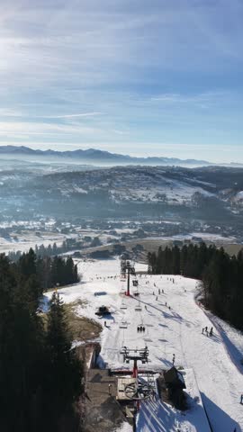 Aerial drone view of Koziniec ski slope on Czarna Gora in Zakopane and Poronin area, showing snowy pistes, skiers, chairlift and panoramic Tatra Mountains landscape on a clear winter day	