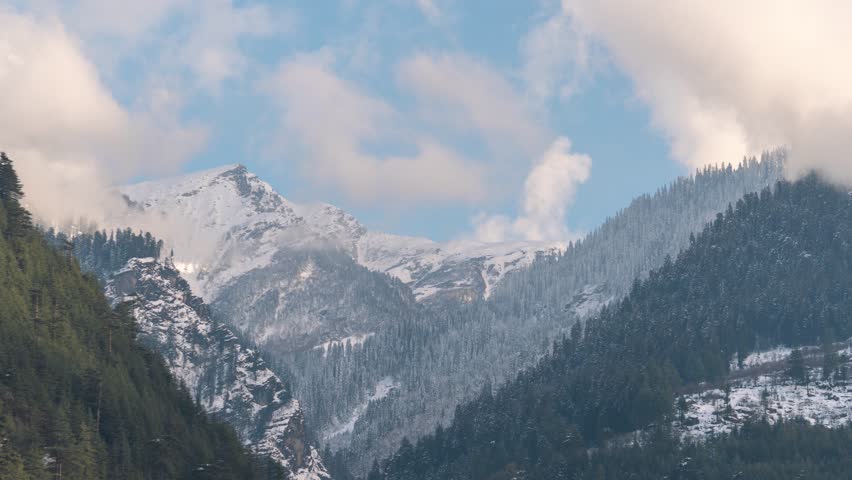 4K Timelapse of clouds in Mountains in Manali with dense coniferous forest and soft sunset light. Fresh snow on mountains during winter season in Himachal Pradesh, India. Foggy landscape creates calm, moody and natural wilderness scenery. Sunset clouds time lapse. Beautiful mountain landscape with clouds and pine trees.
